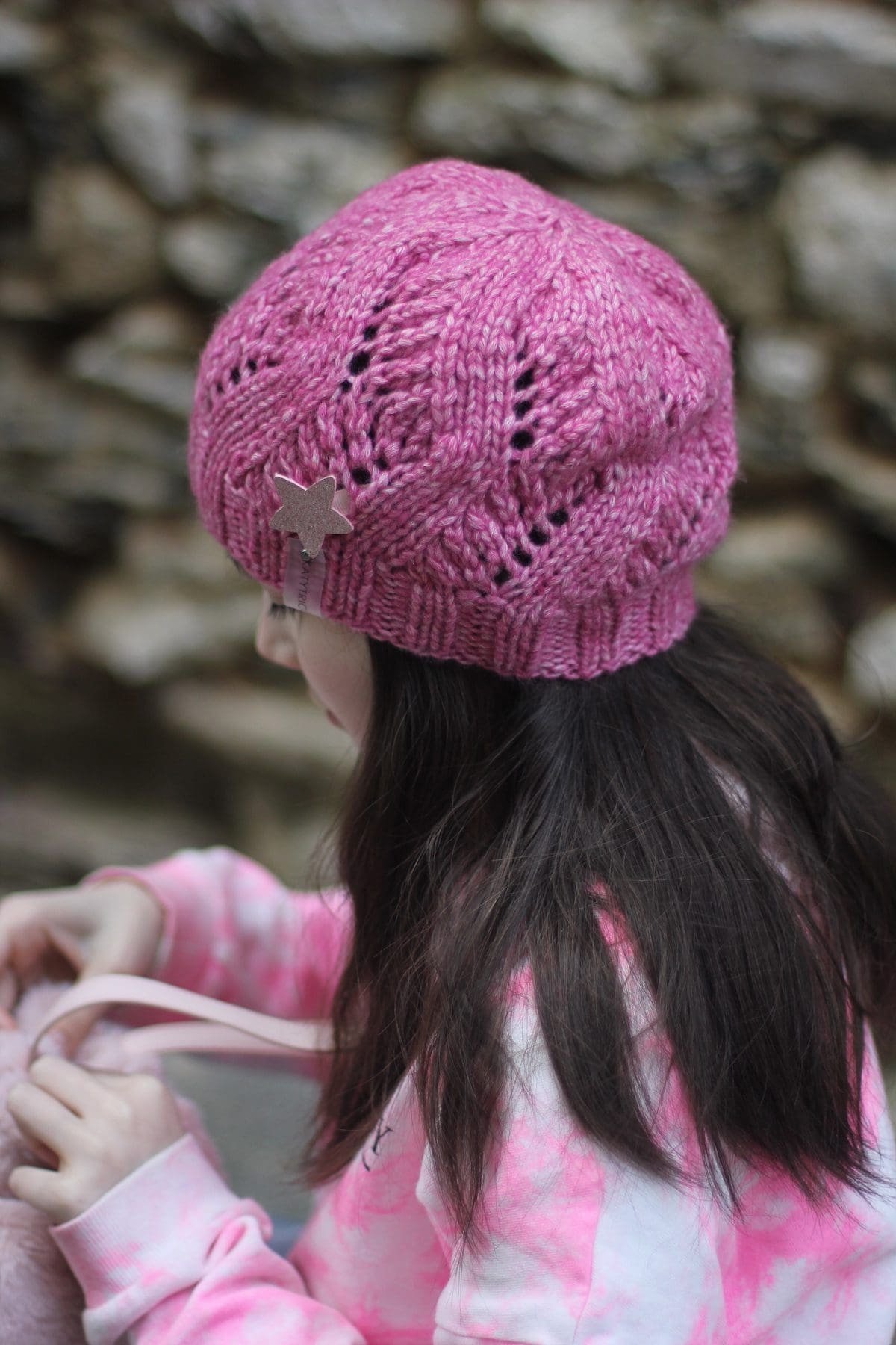 Girl wears a pink knit hat with a star. Winter fashion accessory.