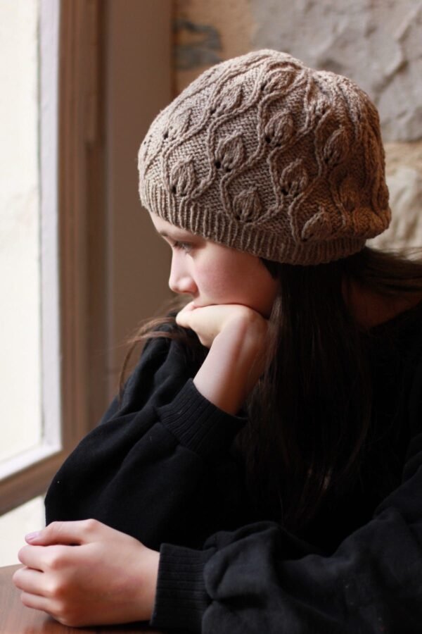 Pensive girl in knit hat looks out window. Portrait of teen deep in thought. Brown hair and cozy winter wear.