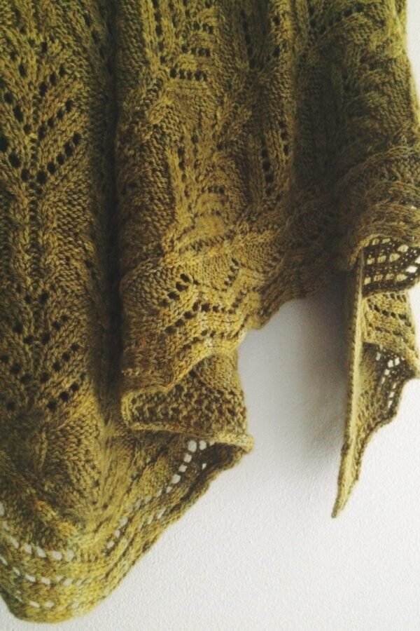 Close-up of forest green knit shawl with lace detailing. Hand-knitted wool garment.