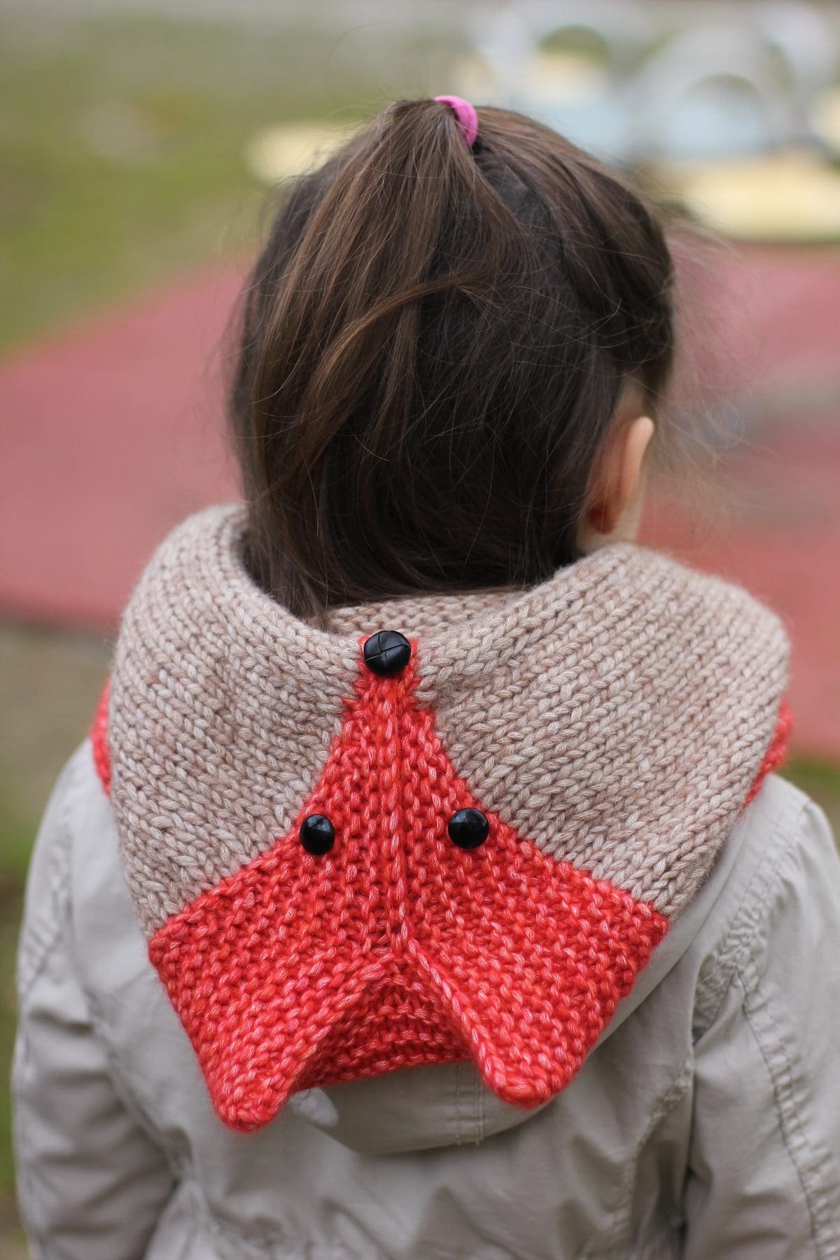 Child wears a knitted cowl. Beige knit with red star design and black buttons. Winter fashion.