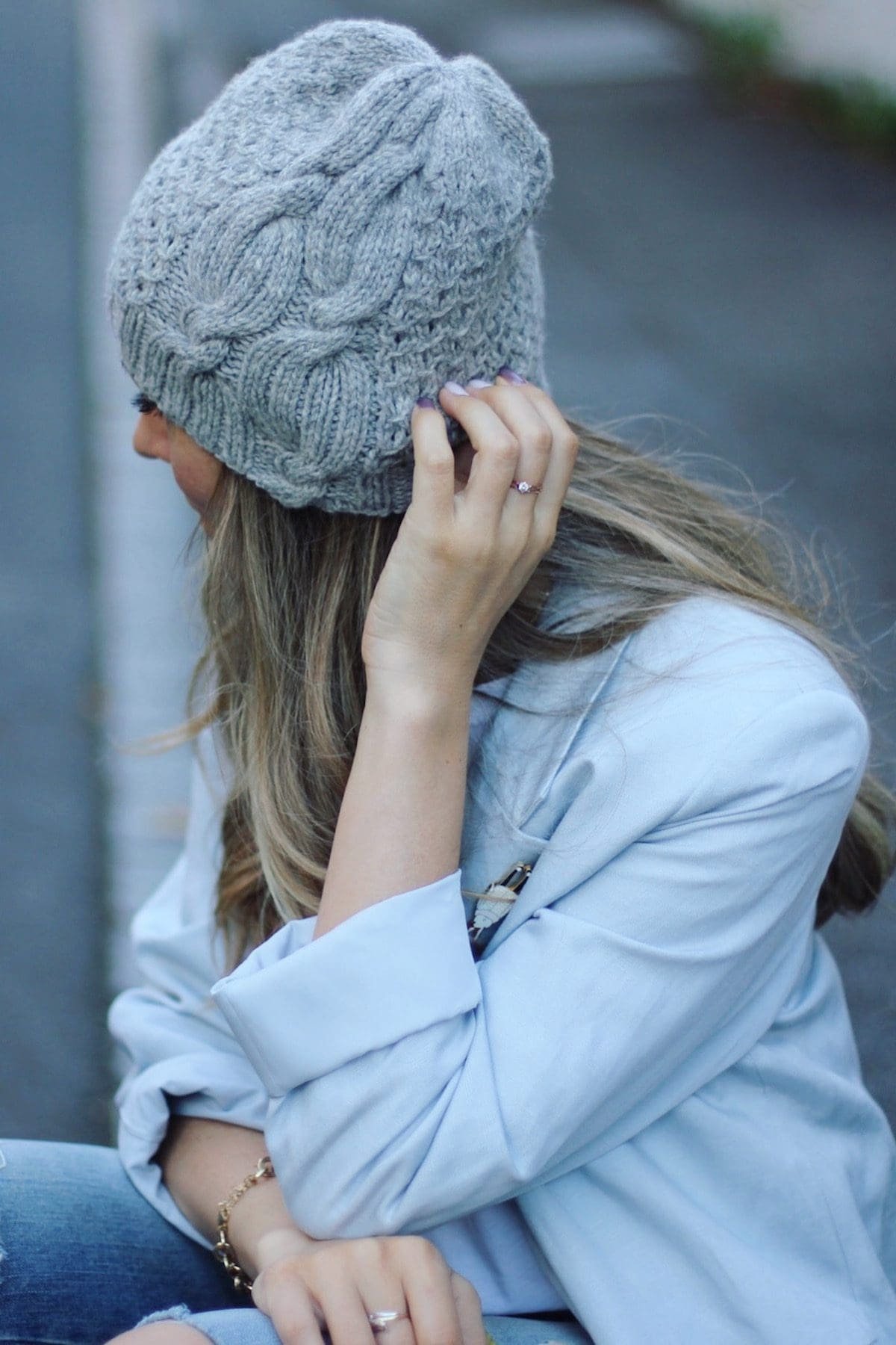 Woman in gray knit hat and blue jacket. Engagement ring on hand. Fashion.