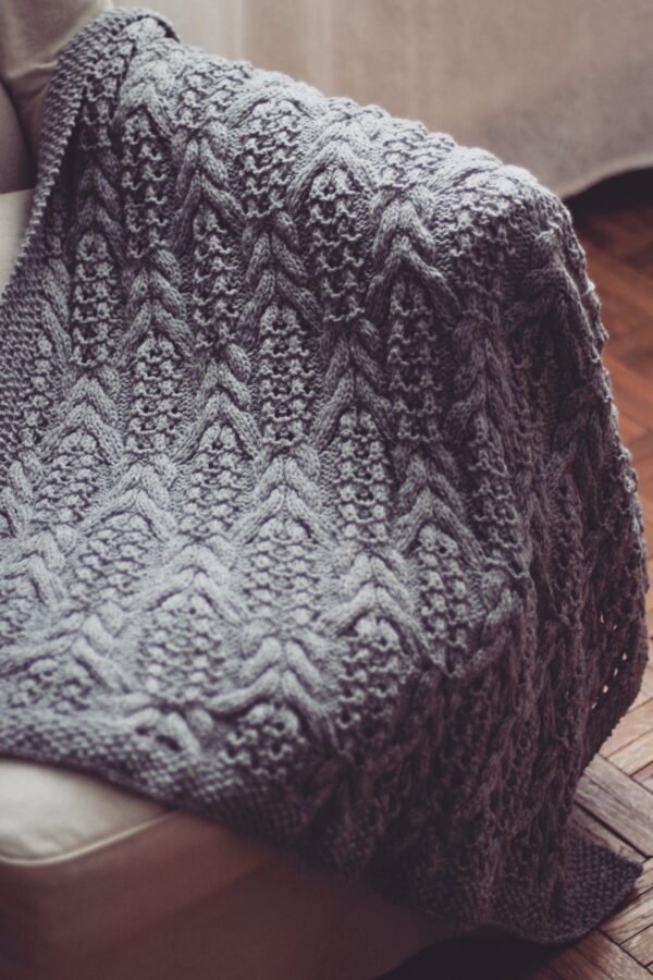 Gray knitted blanket with an intricate pattern. Handmade wool textile, cozy and warm.