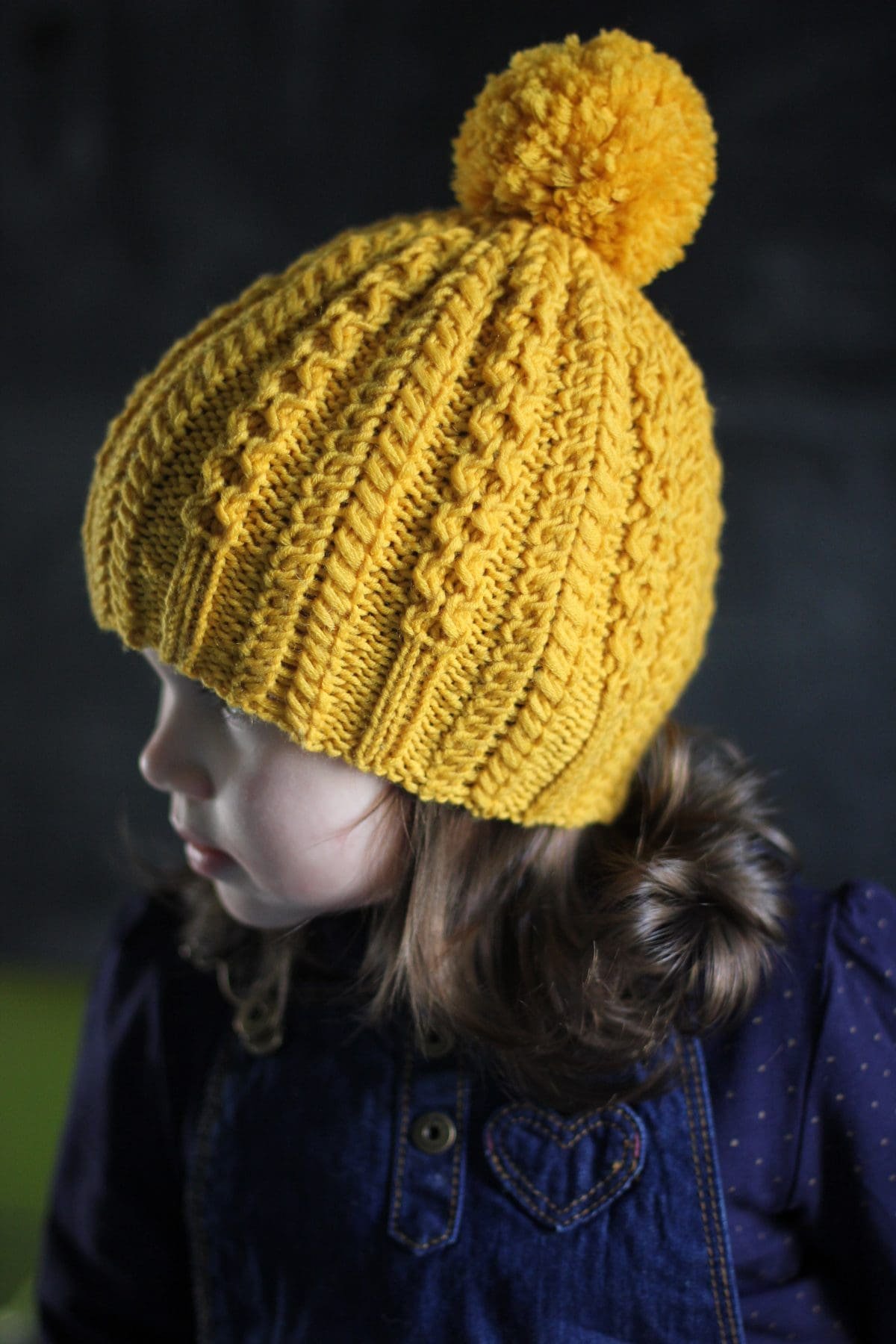 Child wearing a yellow knit hat. Warm winter clothing. Knitted hat with braid pattern.