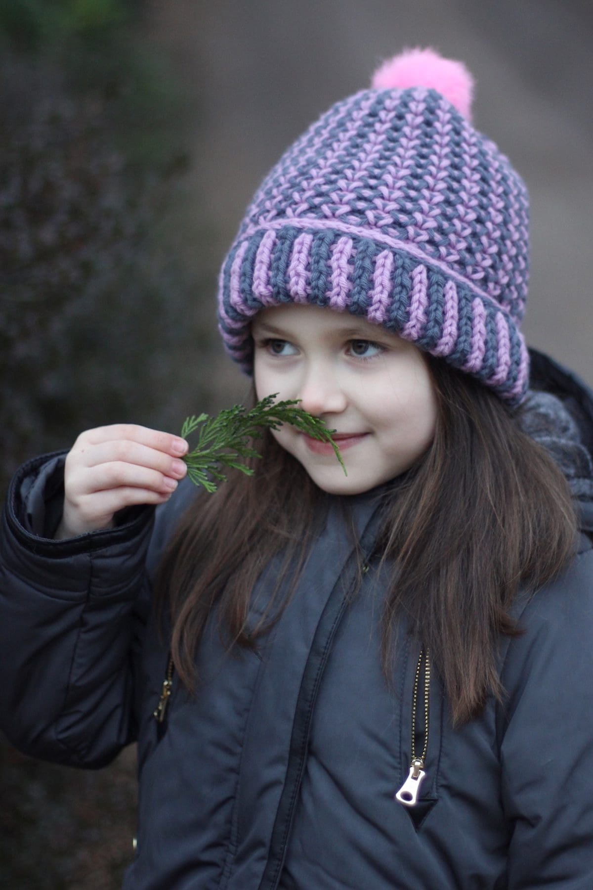 Smiling girl with a leaf mustache. Kid wearing a winter hat and coat. Fun nature activity.