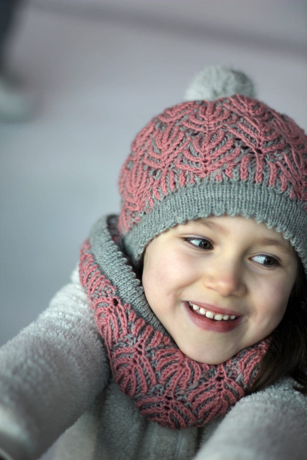 Smiling girl wearing a pink and gray knitted hat and scarf. Winter fashion.