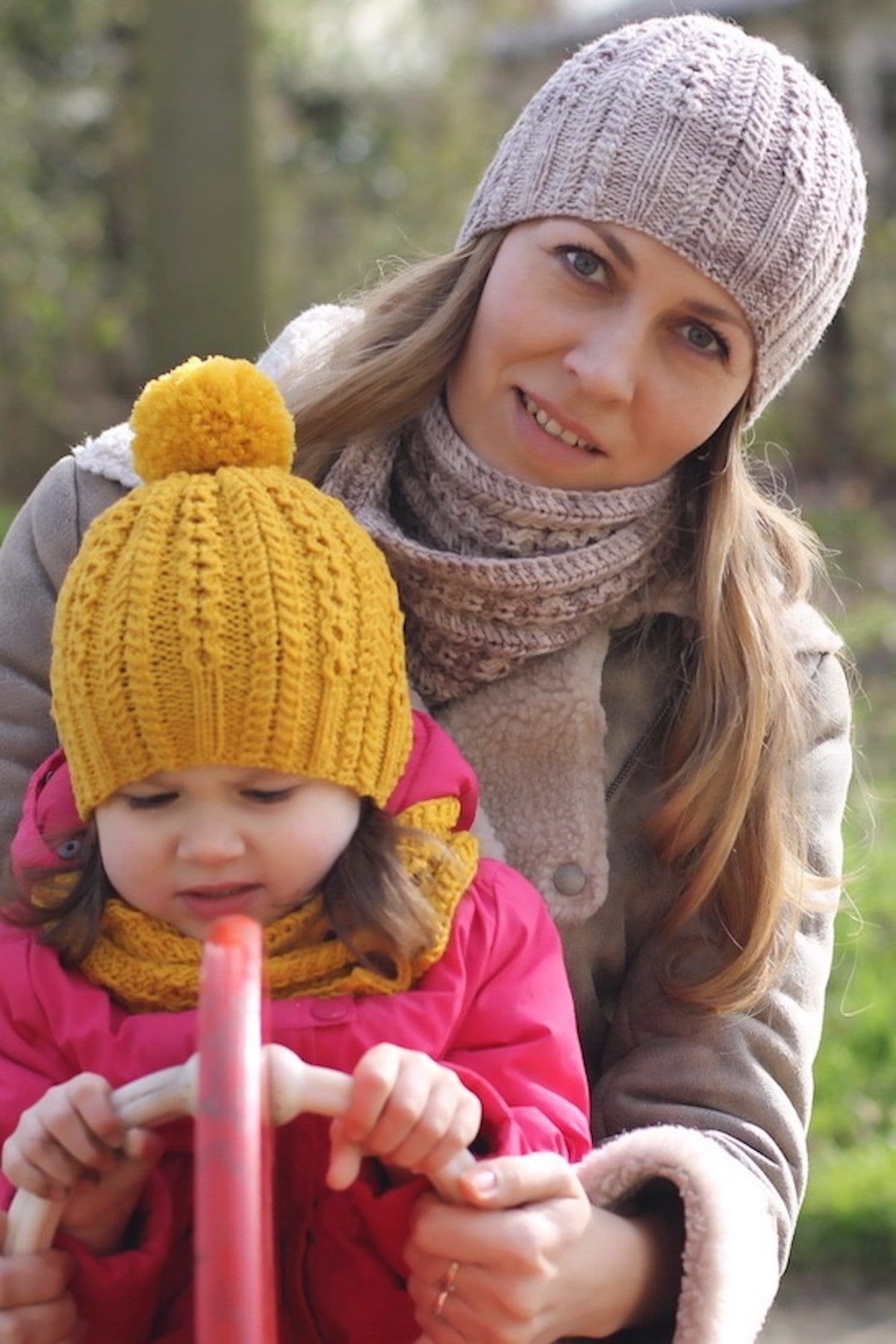 Child in yellow knit hat with pompom and pink jacket. Mother in scarf and coat. Winter fashion.