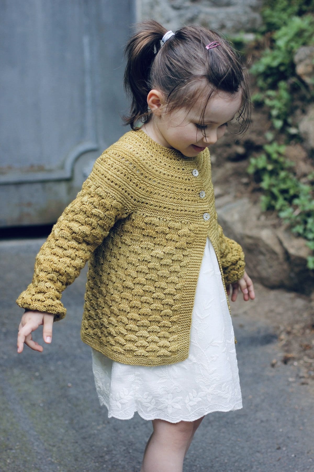 Child in hand-knit cardigan. Textured gold sweater with button closure. Handcrafted knitwear.