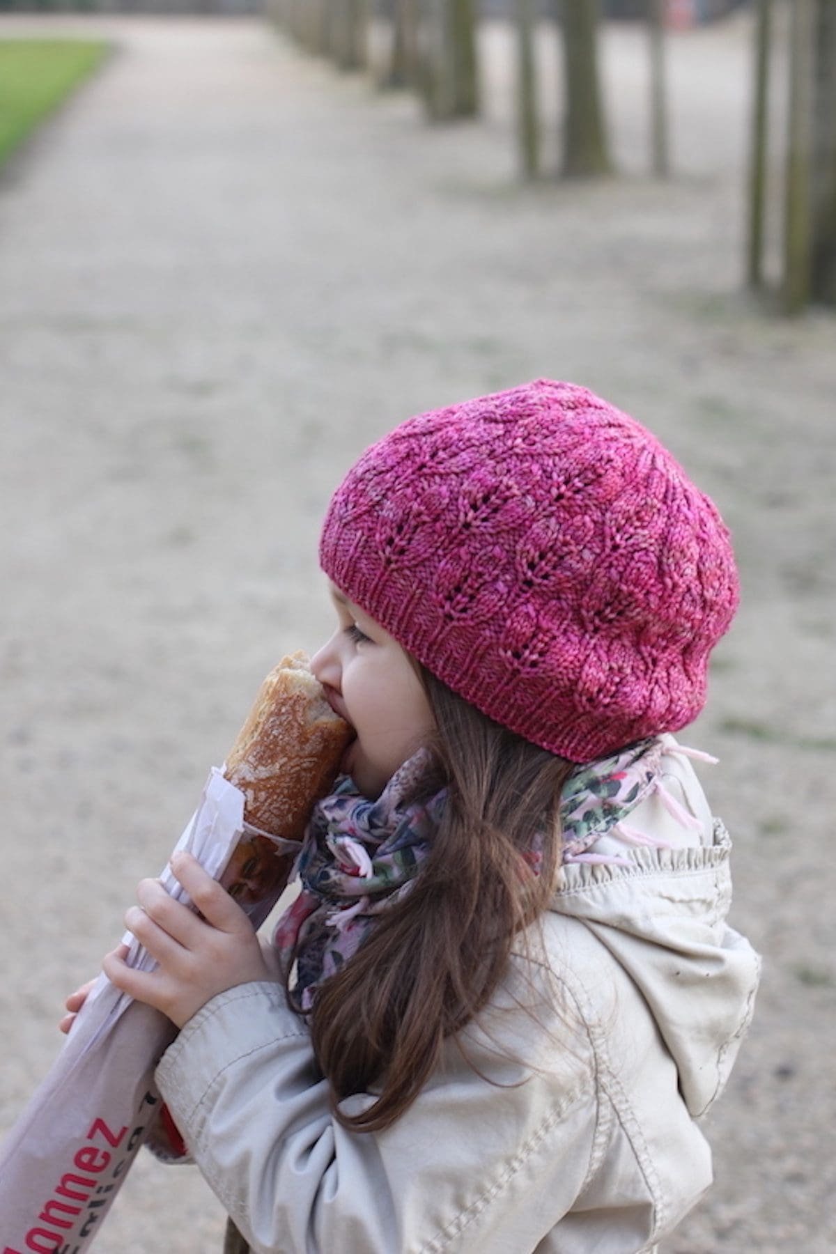 Girl eating baguette, wearing pink knit hat. Casual fashion. Outdoor snack.