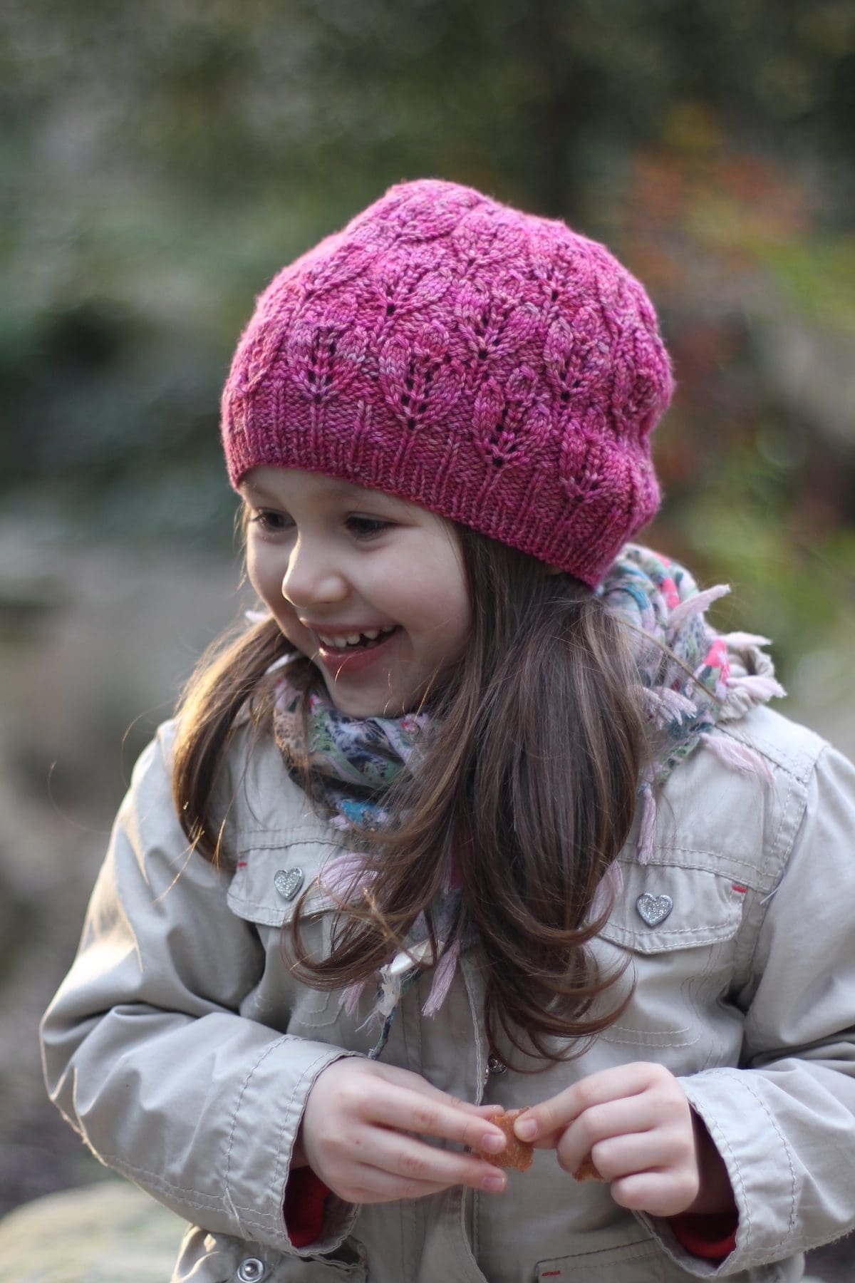 Smiling girl in pink knit hat and scarf. Child portrait, winter fashion.