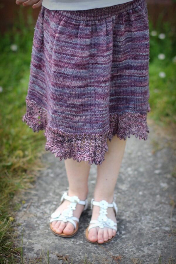 Close-up of a hand-knitted purple dress with lace hem. Knitting pattern, handmade clothing.