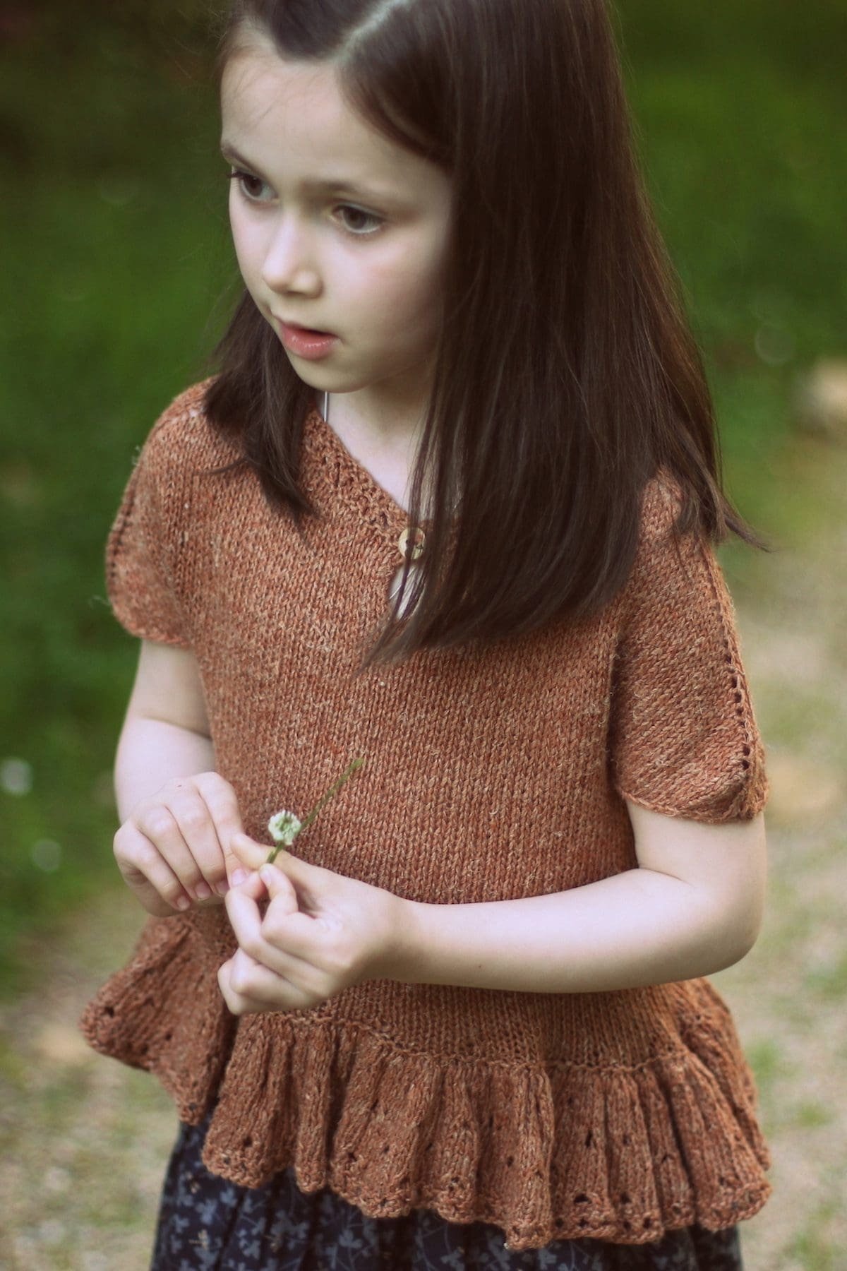 Woman in brown knit top with short sleeves and button detail. Holding small flower. Knitwear fashion.