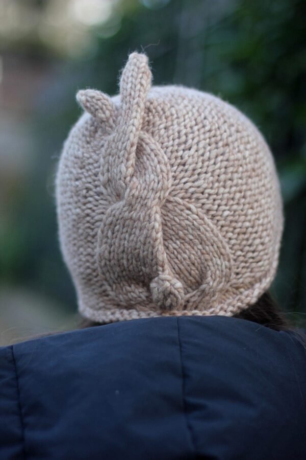 Close-up of a beige knit hat with a bunny tail design. Warm and stylish winter headwear.