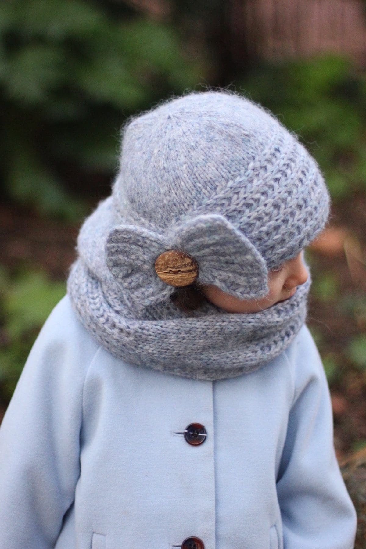 Child in knit hat and cowl with button. Winter fashion, handmade knitwear. Coquette aesthetic.