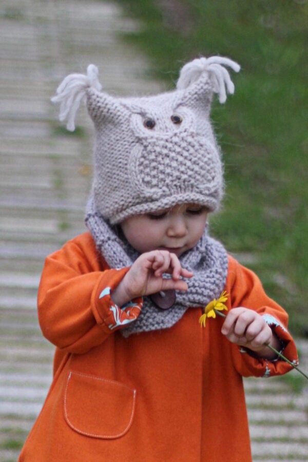 Cute baby girl in knit hat and scarf holds yellow flower. Autumn fashion.