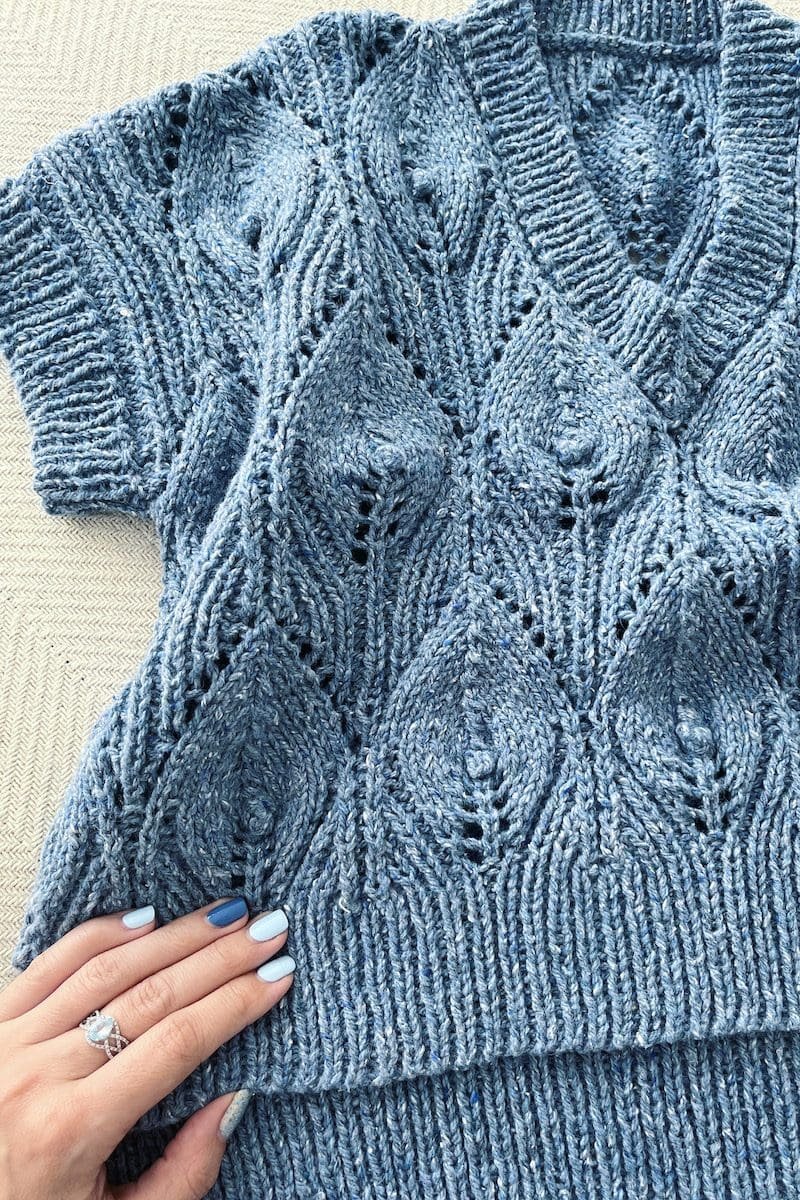 Blue knitted sweater with diamond pattern. V-neck knitwear. Hand with ring and blue nail polish.