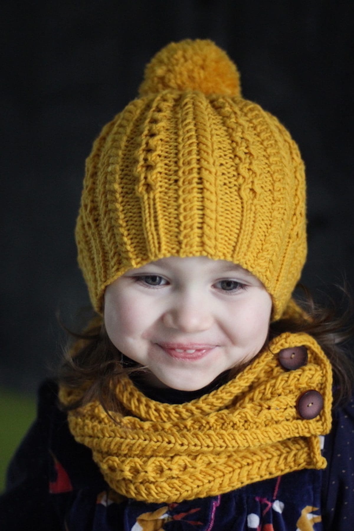 Smiling child wearing a yellow knit hat and scarf. Winter fashion for kids. Cute girl in warm clothing.