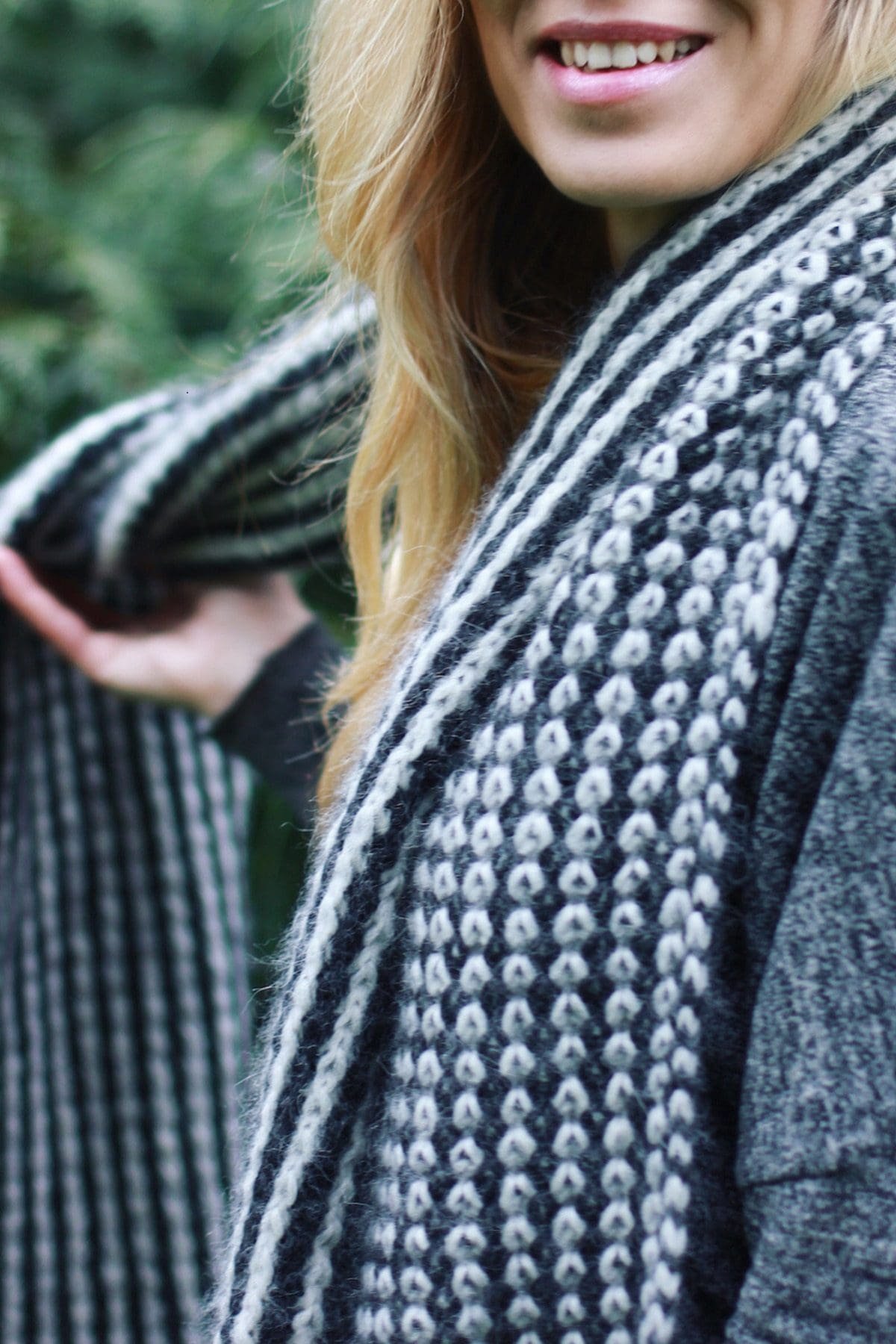 Woman wearing a black and white patterned knit scarf. Fashionable winter accessory.