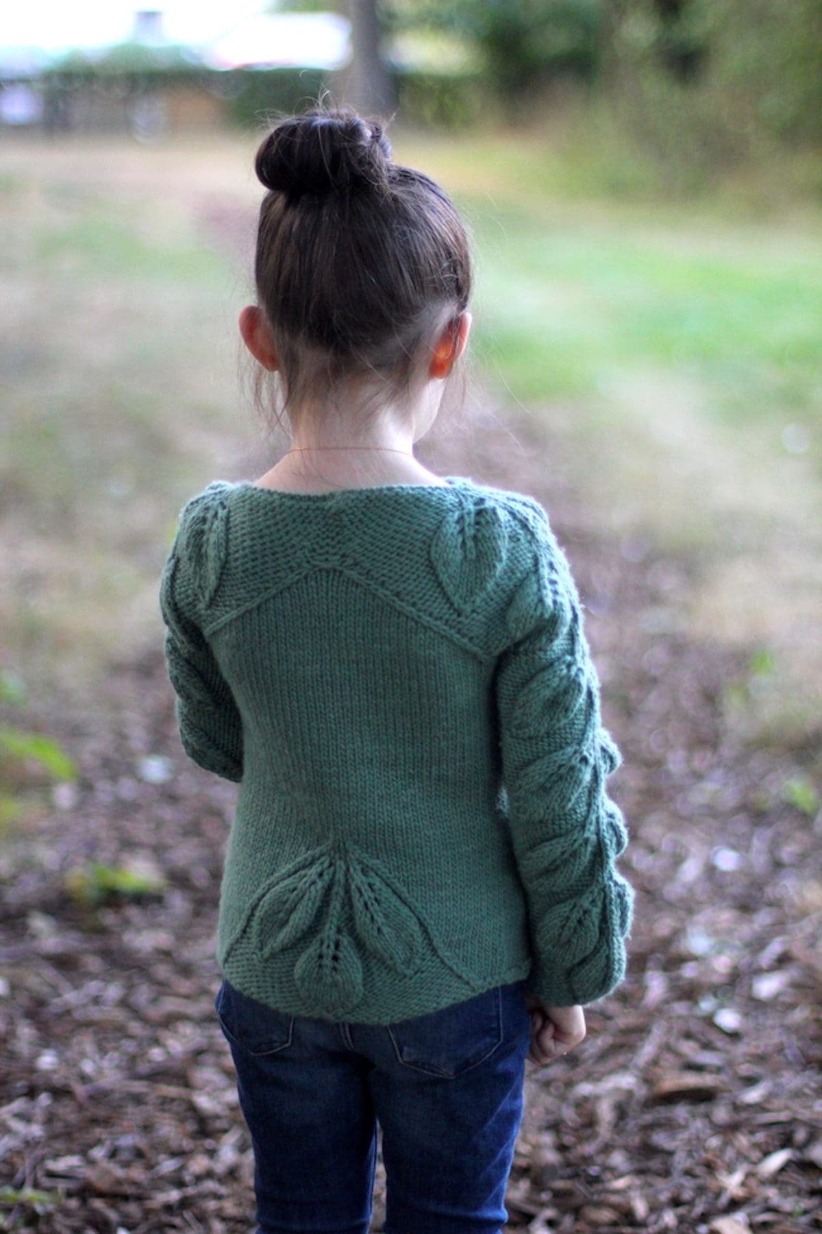 Child wears green knit Beleafme sweater with leaf design. Back view. Fashionable knitwear.