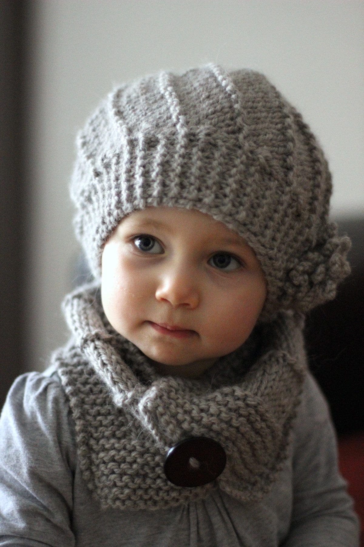 Cute baby girl with blue eyes wearing a gray knitted hat and scarf. Winter fashion.