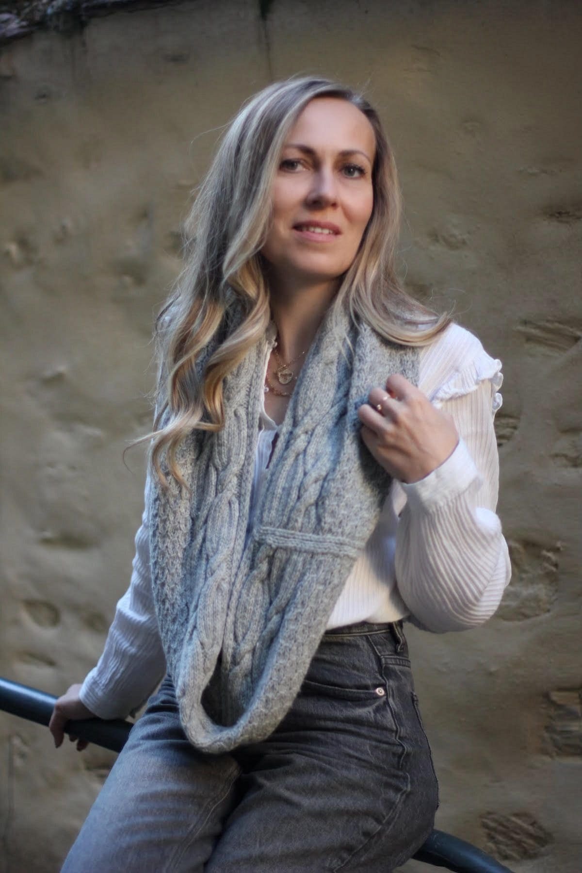 Woman in gray knit infinity scarf and white blouse. Fashionable winter outfit.
