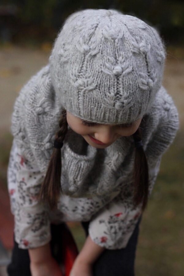 Smiling girl with braids wearing a gray knitted hat and sweater. Winter fashion.