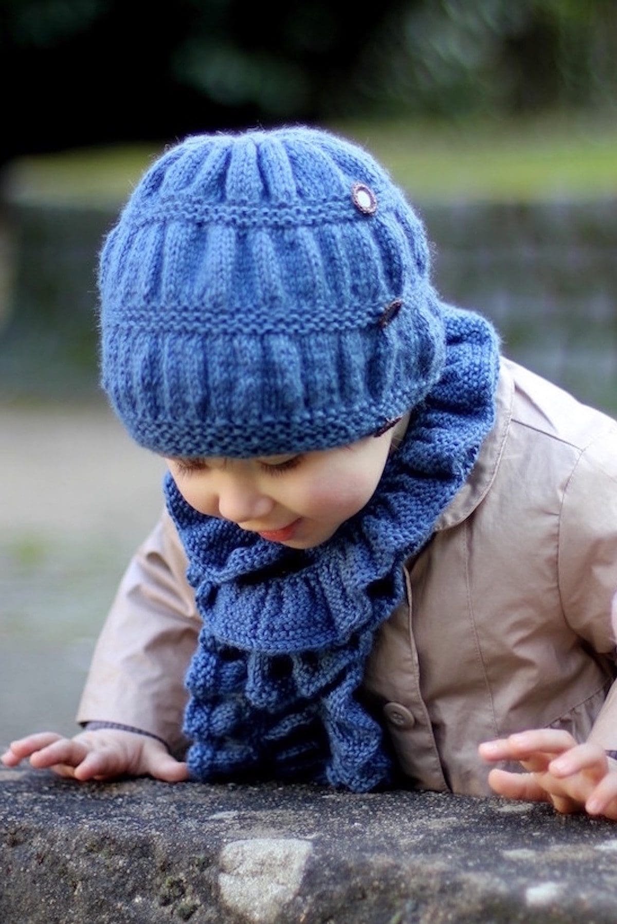 Child in blue knit hat and frill scarf. Winter clothing.