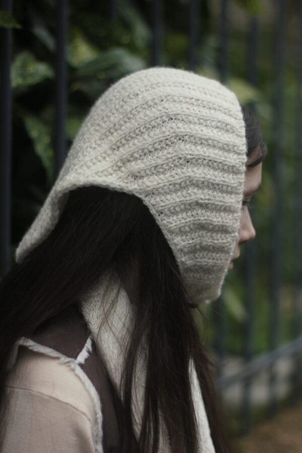 Woman wearing a cream-colored knit hood. Crochet head covering fashion, winter wear.