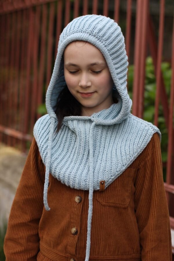 Girl wearing a Nikita Hood. Blue knitted hood with button detail. Winter fashion.