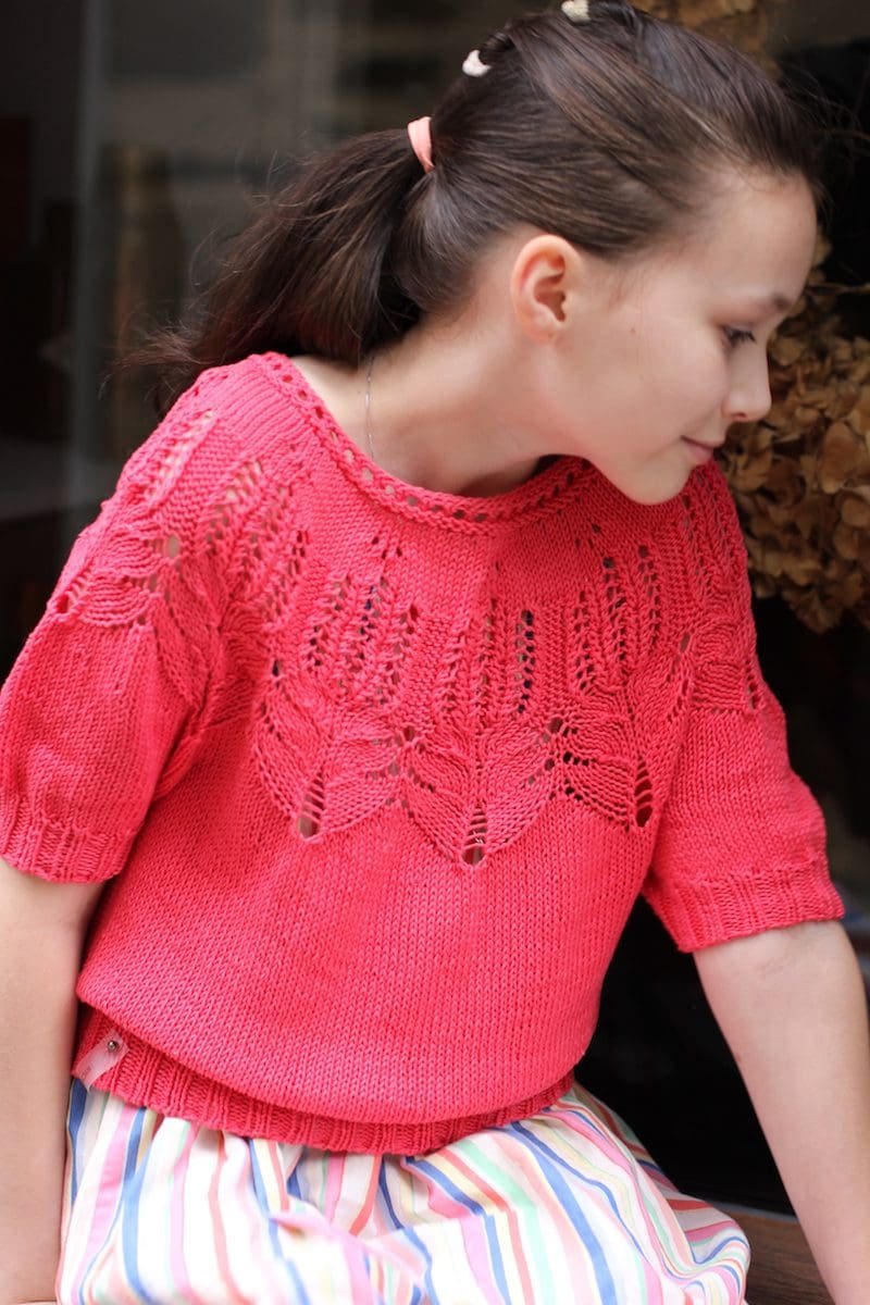 Girl in pink knit tee. Short-sleeved top with leaf-patterned yoke. Striped skirt. Fashionable knitwear.