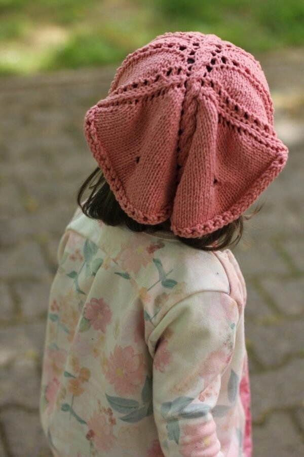 Child wearing a pink knitted sun hat. Cute baby sunbonnet. Kids fashion.