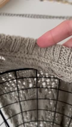Close-up of a diamond vest. Knitted fabric, neutral color. Finger pointing.